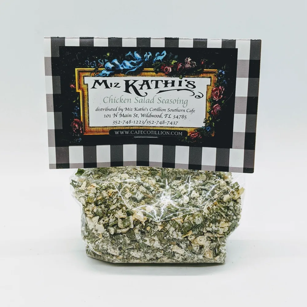 A clear bag of Miz Kathi’s Chicken Salad Seasoning, flecked with dried herbs, under a black-and-white gingham label