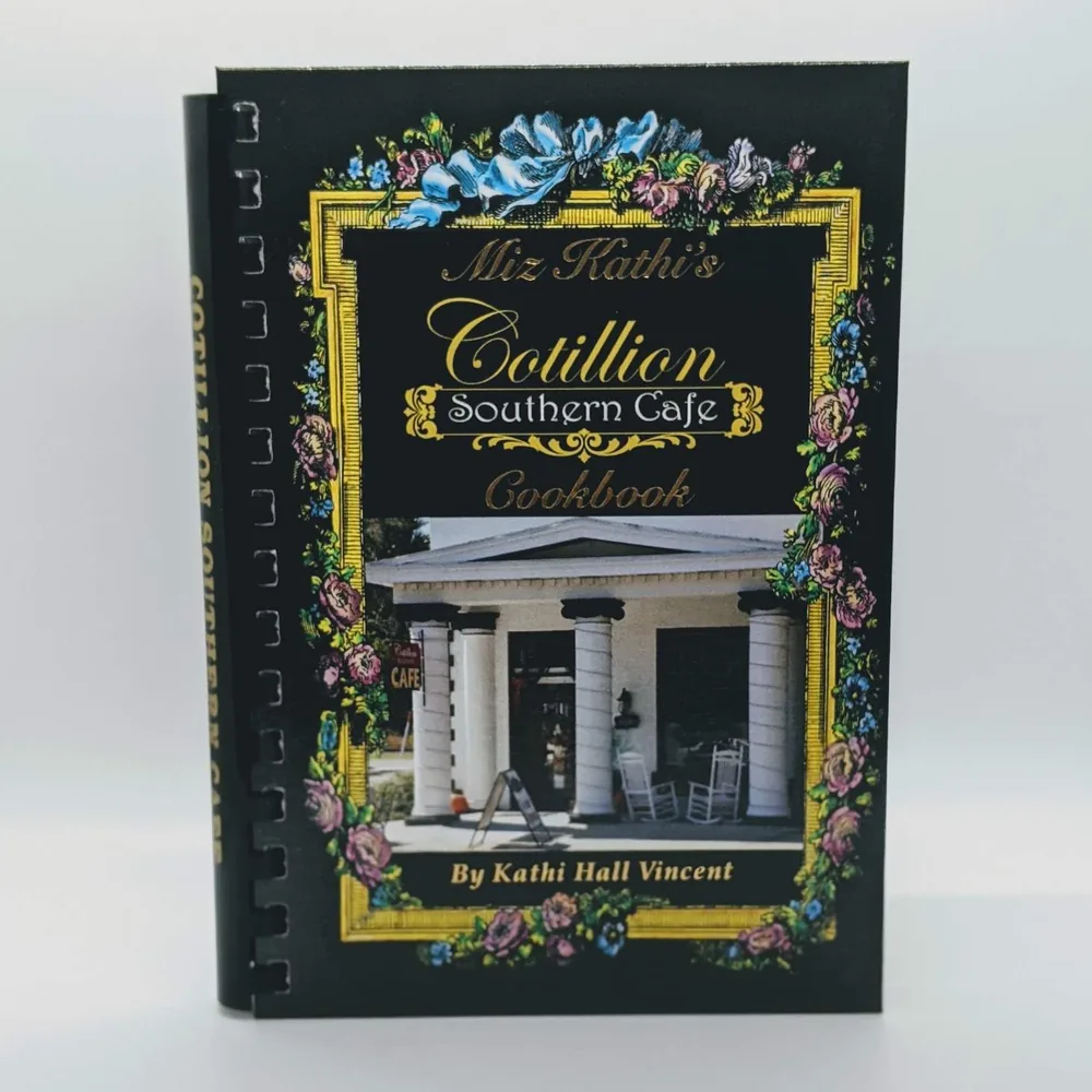 The Miz Kathi’s Cotillion Southern Cafe Cookbook by Kathi Hall Vincent: a spiral-bound book with a black and gold floral cover